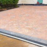 Red and grey block driveway by LevelScape, crafted with Marshalls concrete paving in Brindle and Charcoal, featuring Marshalls kerb stones and cast iron Aco drains.